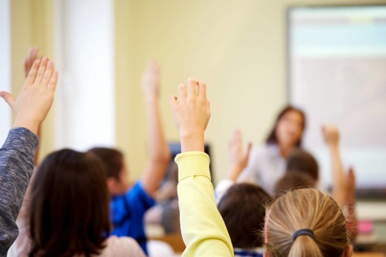 group-of-school-kids-raising-hands-in-classroom-PTEJETQ